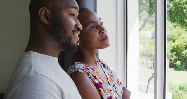 African american couple talking to each other while looking out of the window at home. couple relationship lifestyle concept