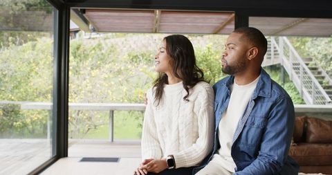 Couple sitting on sofa looking out glass wall to deck wearing smartwatch and cozy knit sweater