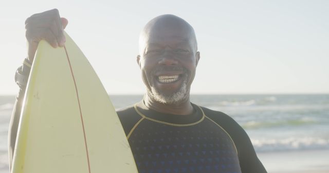 Portrait of happy senior african american man carrying surfboard on sunny beach at sunset,copy space. Retirement, sport, hobbies, summer, vacations and active senior lifestyle, unaltered.