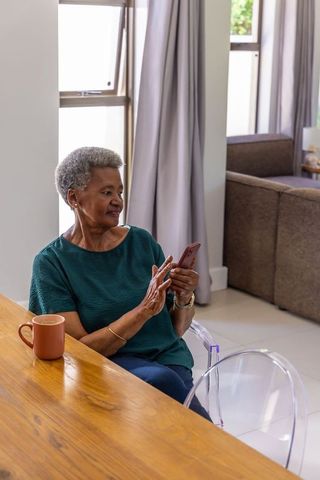 Senior african woman using smartphone at home with coffee on wooden table, morning routine