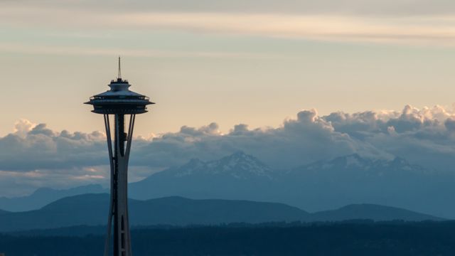 Seattle Space Needle stands tall against dusky sky with mountain range in distance. Ideal for showcasing Seattle's iconic architecture, promoting tourism, or emphasizing city's scenic beauty and famous landmarks.