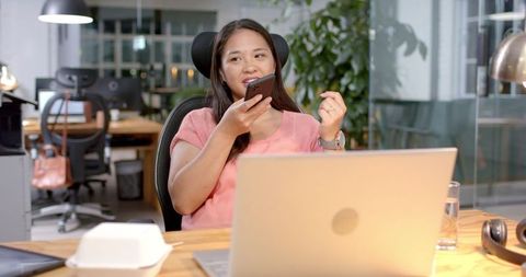 Asian Businesswoman Recording Voice Note in Modern Office Scene