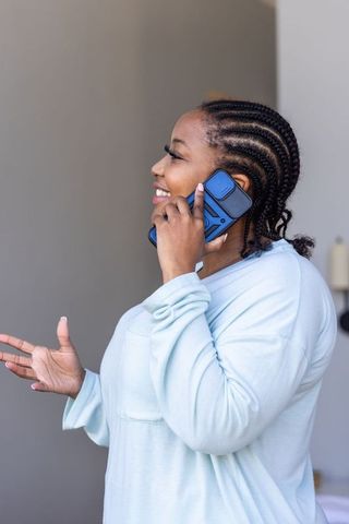 African american woman smiling while talking on blue smartphone at home