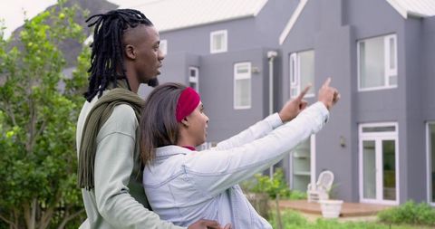 Diverse couple pointing at new townhouse during home tour on front lawn