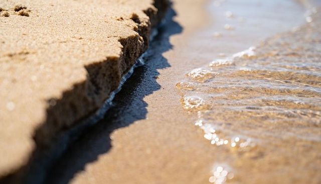 Eroding sand ledge with gentle wavelets closeup minimalist beach texture serene shoreline
