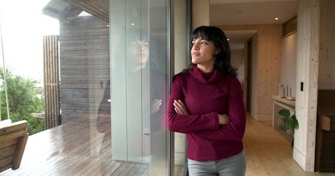 Woman reflecting indoors by glass door with deck view
