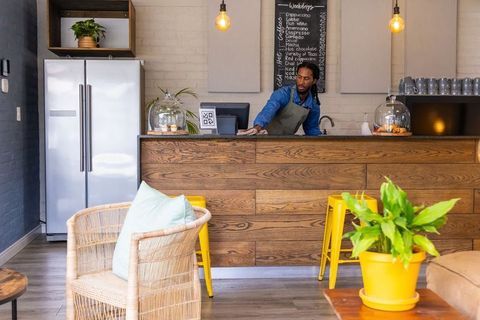 African american barista serving at rustic coffee counter, pastries and chalkboard menu