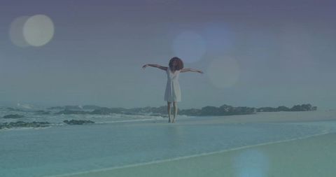 Balancing woman in white dress stretching arms on tidal pool shoreline