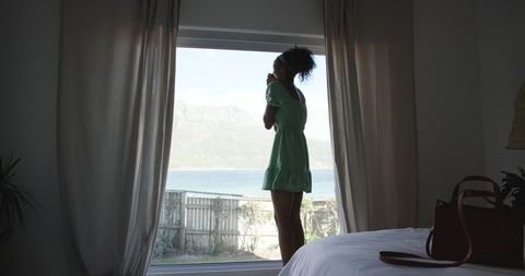 Woman in green dress gazing out of bedroom window at scenic view