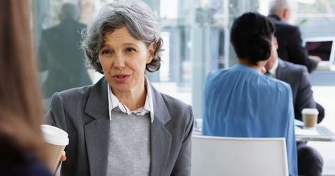 Professional senior businesswoman having coffee and discussion in modern cafeteria