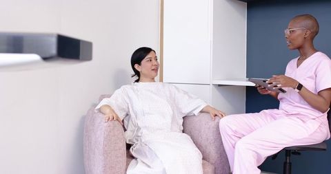 Diverse female patient consulting nurse with tablet in modern clinic