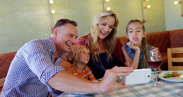 Father and mother with daughter and son taking a cheerful selfie at a family dinner. Daughter is making a funny face, adding humor and joy to the moment. Perfect for use in advertisements, blogs, and social media posts related to family bonding, dining out, and creating memories with loved ones.