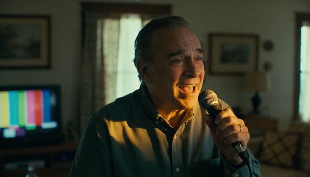Senior man singing into microphone at home with tv test bars, warm cozy interior
