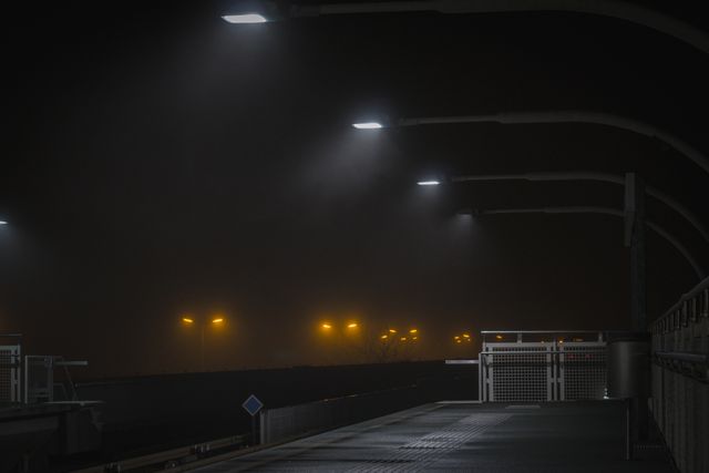 Image depicts an empty train station platform illuminated by bright LED lights, contrasting with distant streetlights. Ideal for use in urban themes, moody scenes, transportation-related articles, or illustrating solitude and quietness in city life.