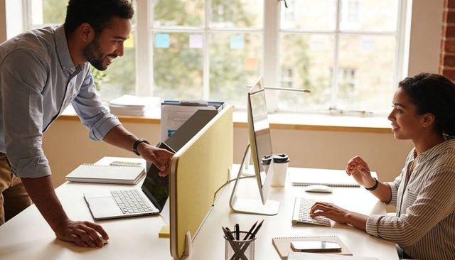 Colleagues collaborating across modern workspace, man pointing at monitor while woman typing
