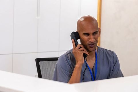 African american male clinic receptionist answering phone at modern medical front desk