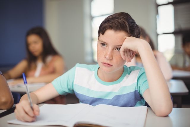 Tensed school boy doing homework in classroom at school