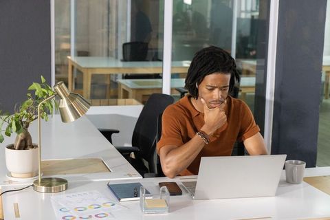 African american professional working focused at modern coworking desk with laptop and smartphone