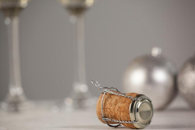 This image features a close-up of a champagne cork with Christmas decorations in the background, including blurred wine glasses and silver ornaments. Ideal for holiday celebration themes, party invitations, festive advertisements, and New Year promotions.