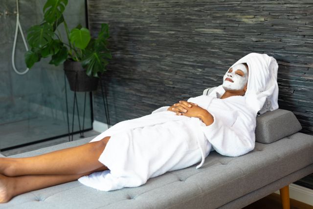 Young african american woman in bathrobe and head towel with spa face mask relaxing at home. Unaltered, copy space, spa, relaxation, pampering, detox, body care and wellbeing concept.