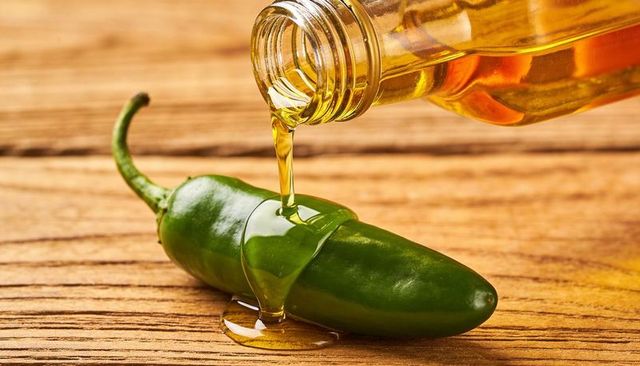 Drizzling golden oil over green jalapeno pepper on rustic wooden surface
