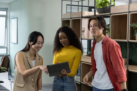 Young professionals collaborating over tablet in modern office with plants and shelving