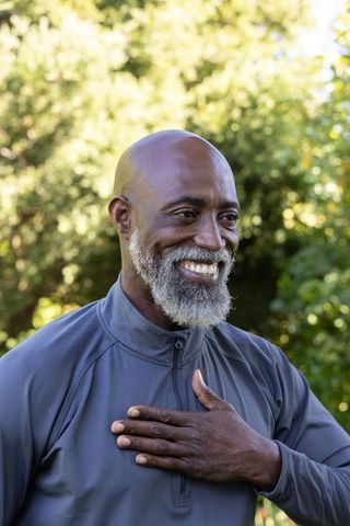 Senior african american man smiling outdoors holding hand over chest expressing gratitude
