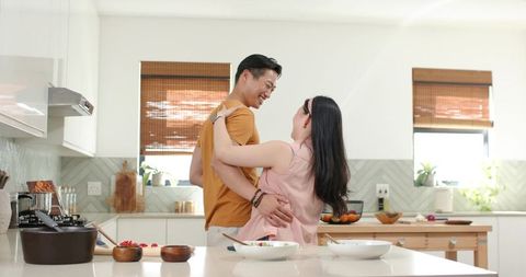Intimate couple embracing while preparing meal at bright modern white kitchen island
