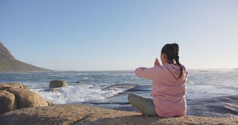 Woman Meditating on Rocks by Sea in Morning Meditation Pose