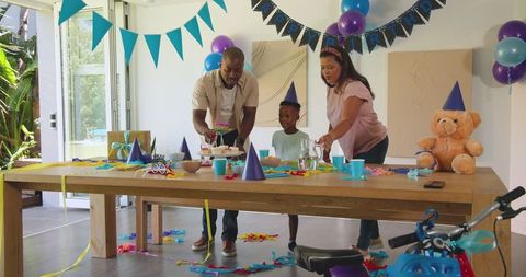 Family Celebrating Child's Birthday with Cake and Banners at Home