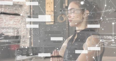 Woman studying multiple monitors with futuristic HUD overlays in industrial workspace