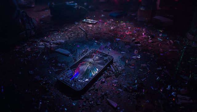 Cracked smartphone reflecting purple neon shards on dark floor among confetti