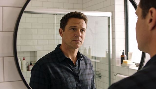 Midlife man studying reflection in round mirror in modern tiled bathroom with window light