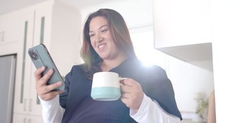 Smiling Plus Size Female Doctor Enjoying Coffee While Using Smartphone