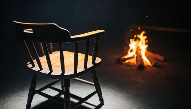 Wooden spindle-back chair facing campfire on packed earth at night with warm firelight