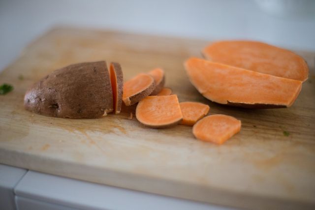 Close-up view of sweet potato slices on a wooden chopping board. Ideal for illustrating topics related to healthy eating, meal preparation, vegetarian diets, and farm-to-table concepts. Perfect for food blogs, recipe books, and cooking websites.
