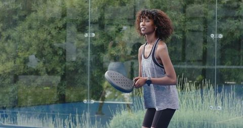 Young african american woman playing padel on glass court with smartwatch and athleticwear