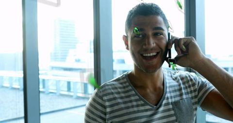 Smiling Man in Casual Tee Calling Near Office Windows with Graphics