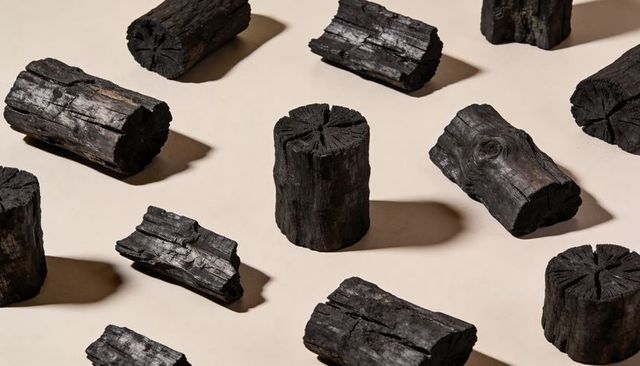 Charcoal logs arranging on beige tabletop casting dramatic shadows and bold texture