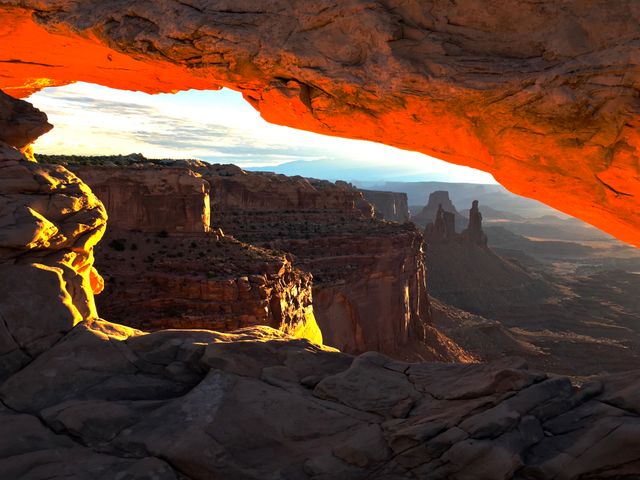 Dramatic image captures the intense orange glow of the sunrise illuminating Mesa Arch in Canyonlands National Park. Implies a sense of awe and grandeur. Ideal for nature, travel, and tourism promotions, online articles about national parks or Southwestern landscapes, desktop wallpapers, and posters promoting natural wonders.