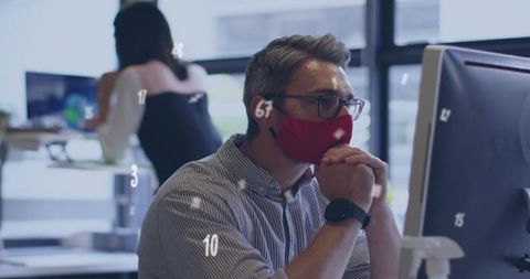 Office professional wearing red face mask focusing on monitor during collaborative work