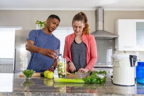 Healthy lifestyle couple preparing green smoothie in modern kitchen, pouring and chopping