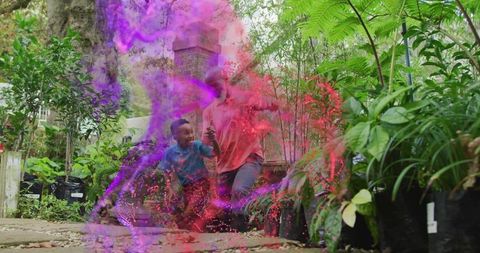 Grandparent crouching with grandchild spraying magenta powder in lush garden nursery