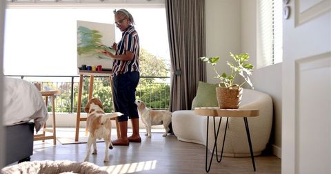 Senior Woman Painting at Home with Dogs Nearby
