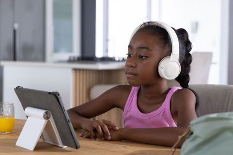 African american girl wearing headphones using tablet at home studying and learning