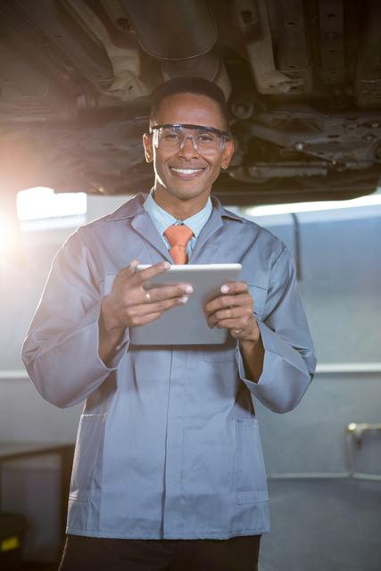 Mechanic in uniform using a digital tablet while standing in a repair garage, suggesting modern technology in automotive repair. Perfect for illustrating advanced automotive services, digital tools in repair shops, and modern mechanics at work.