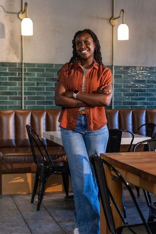 African american woman standing arms crossed smiling in modern cafe with green tiled wall