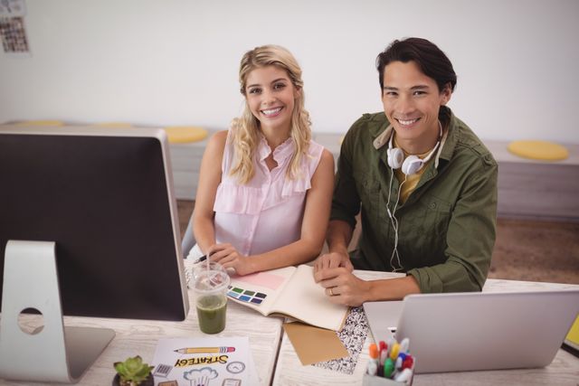 Portrait of smiling young coworkers working together at creative office desk