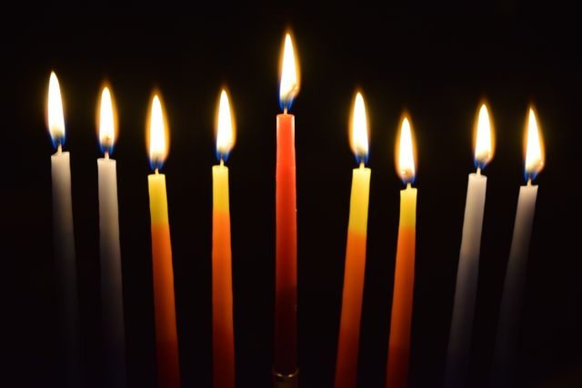 Colorful, lighted Hanukkah menorah with nine candles, centrally positioned on dark background. Ideal for illustrating Hanukkah celebrations, Jewish traditions, religious holidays, and cultural festivals. Suitable for articles, holiday cards, educational materials, and event promotions.