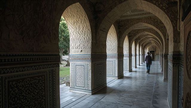 Man walking along marble arched colonnade revealing courtyard and ornate tiled corridor